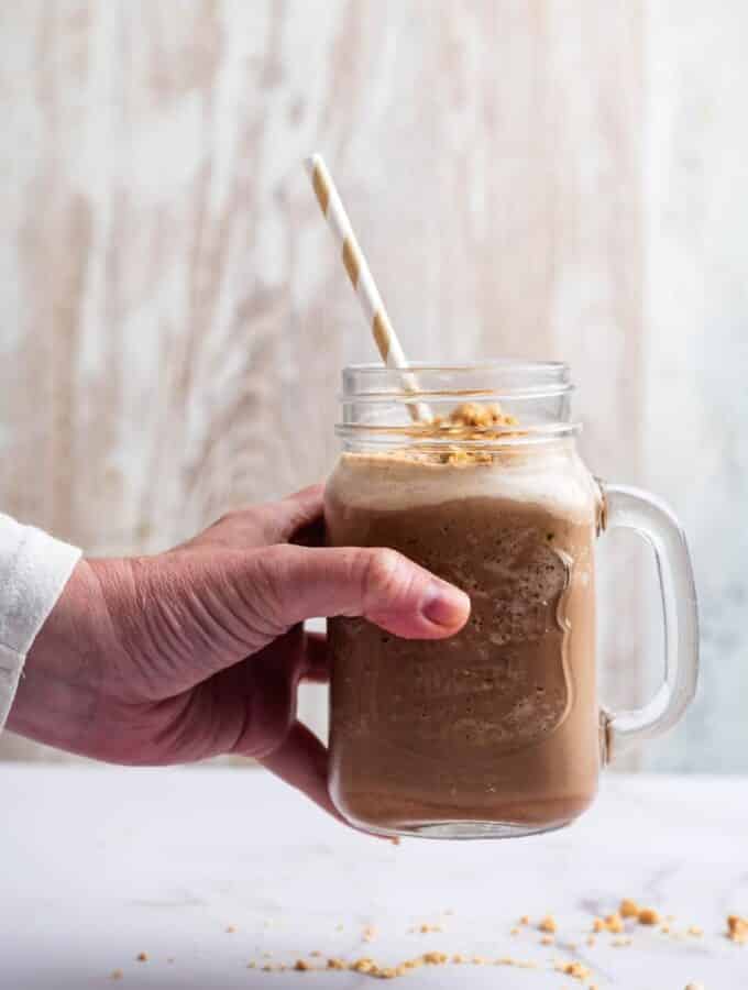 A hand holding a glass mug that is filled with a keto protein shake.