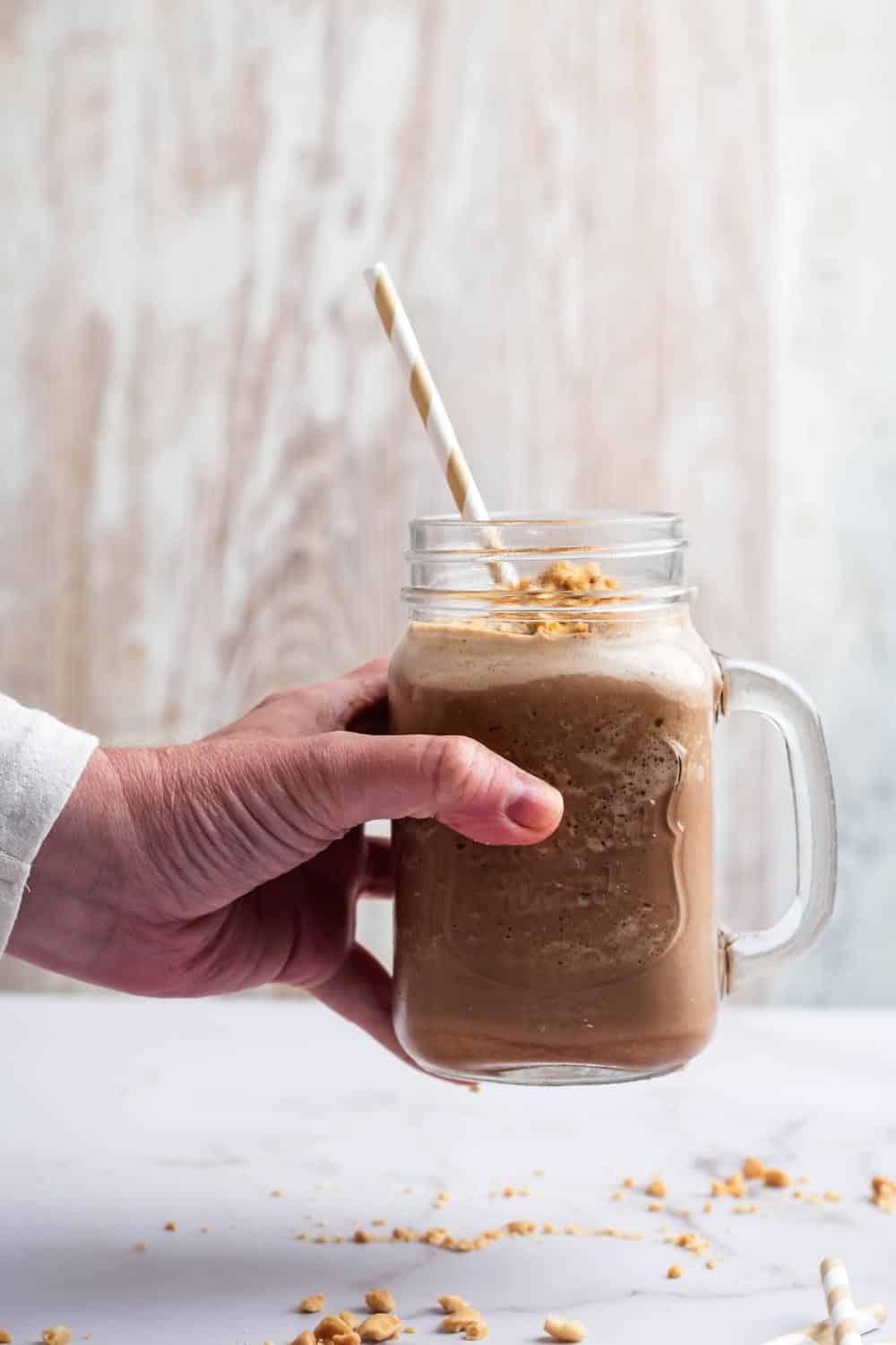 A hand holding a glass mug that is filled with a keto protein shake.