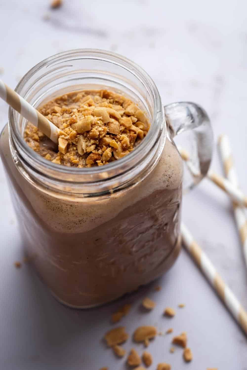 A glass mug with a keto smoothie in it with crushed peanuts on top.