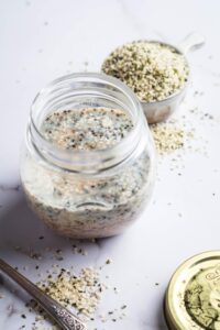 Keto overnight oats in a glass jar on a white counter. Behind it is a cup filled with some Chia seeds and flaxseeds.