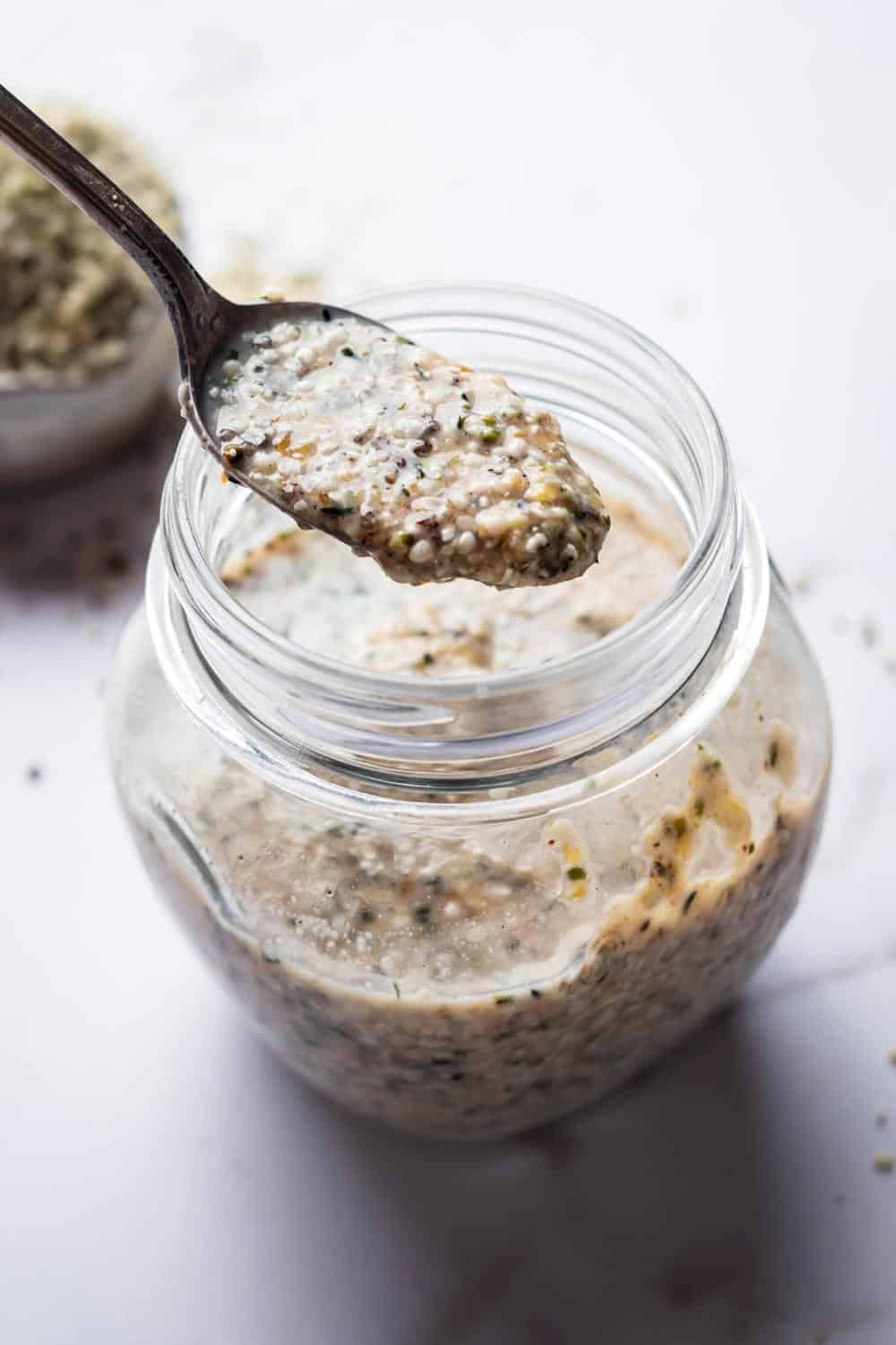 A spoon with keto overnight oats on it above a glass jar that is filled with the keto overnight oats.
