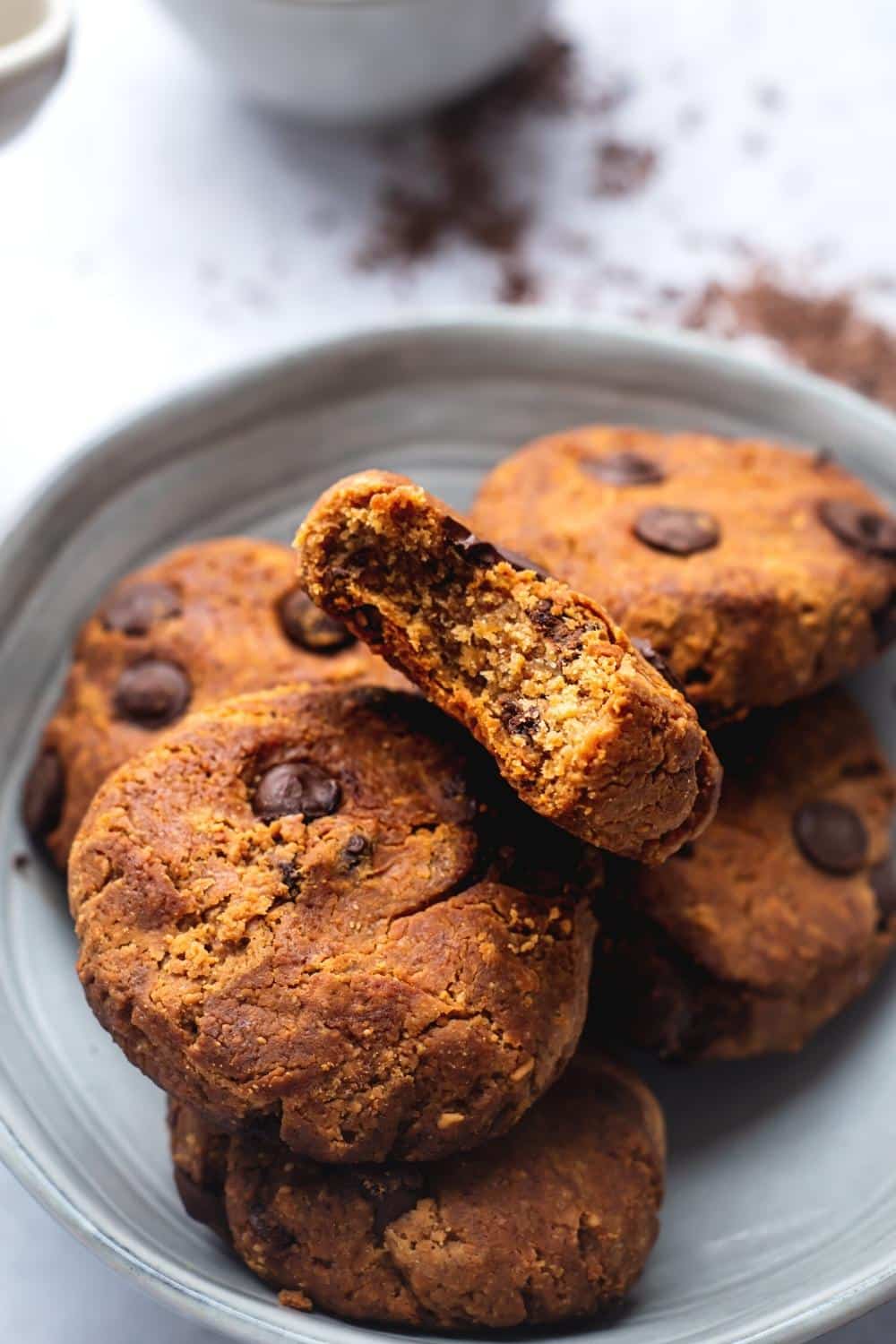 A bitten protein cookie on top of more peanut butter protein cookies in a bowl.