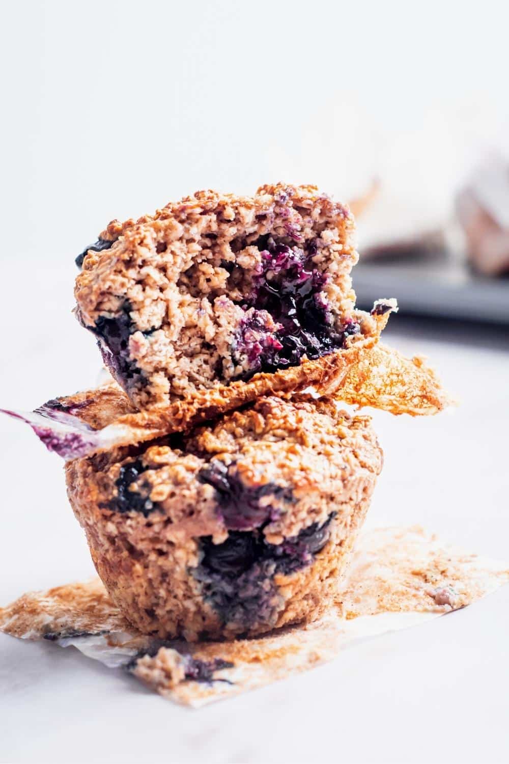 Two blueberry protein powder muffins on top of one another. the top muffin has a bite out of the front.