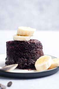 Two banana slices on top of a chocolate protein mug cake and a white plate.