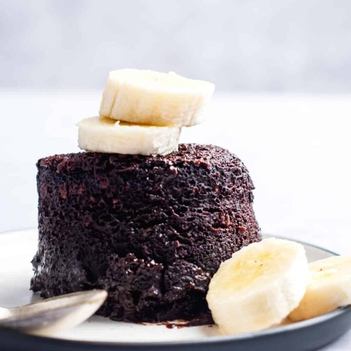 Two banana slices on top of a chocolate protein mug cake and a white plate.