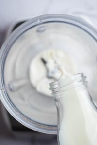 A glass pouring milk into a blender.