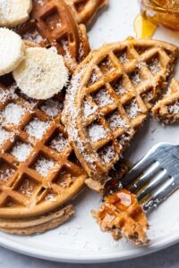 Half of a protein waffle and part of another protein waffle on top of a white plate.