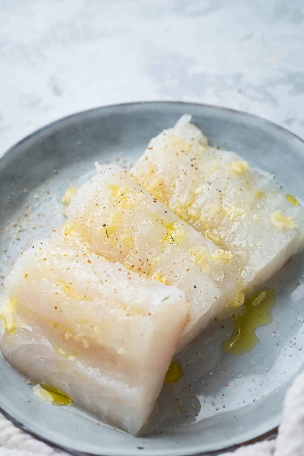 A halibut fillet coated in olive oil on a grey plate.