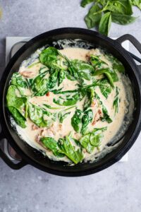 Spinach, sun dried tomatoes, and a cream sauce in a pot.