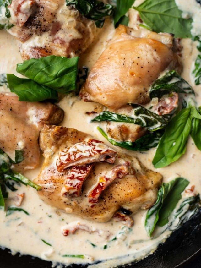 Sun dried tomatoes on a chicken thigh that is in a cream sauce with spinach in a pot.
