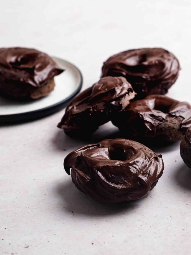 Four chocolate glazed protein donuts on a white counter.