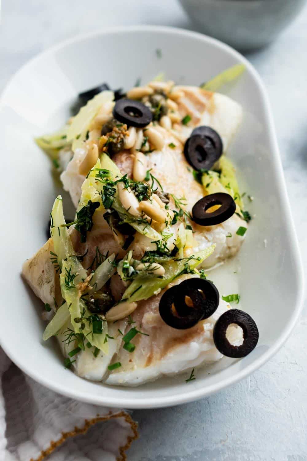 A bunch of pine nuts, black olives, and celery on top of halibut fillets.