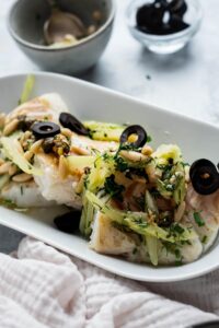 A few pan seared halibut fillets covered in black olive, celery, and pine nuts.