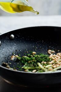A skillet with pine nuts, dill, celery, and olive oil.