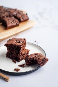 A plate that has two brownies on top of one another and another brownie with a bite out of it.