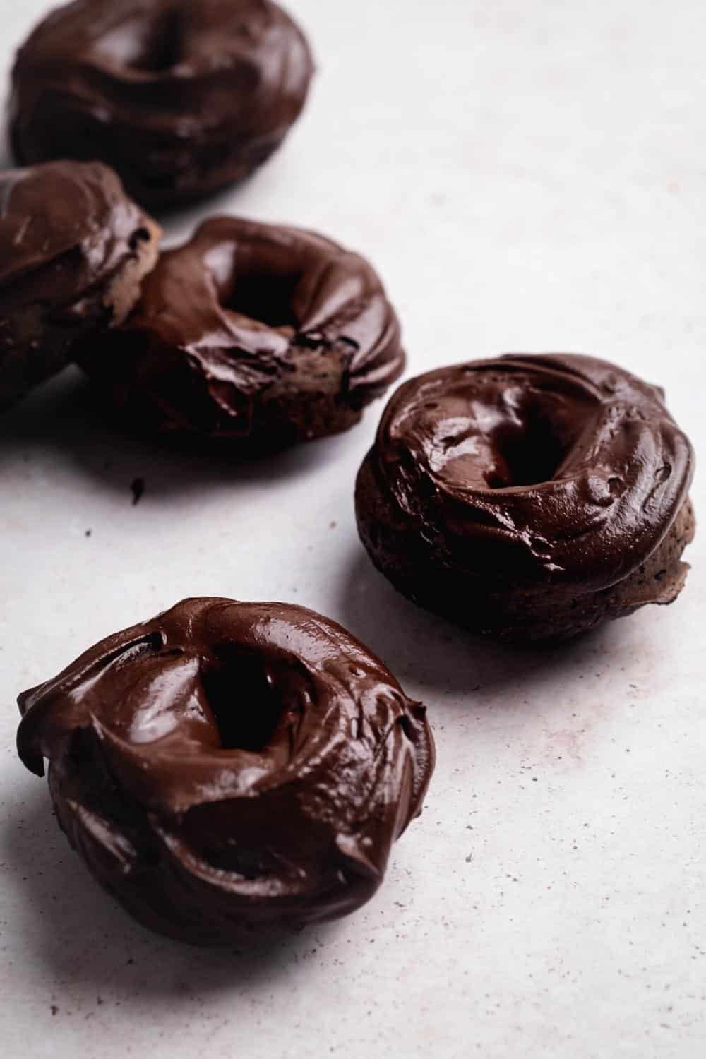 Five chocolate protein donuts scattered on a white counter.