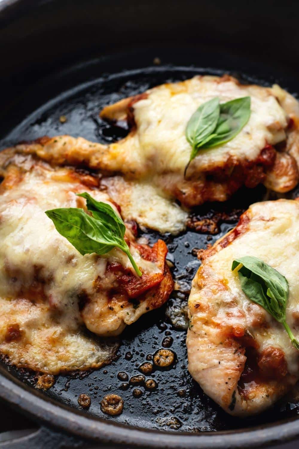 Three pieces of keto chicken parmesan in a black skillet.