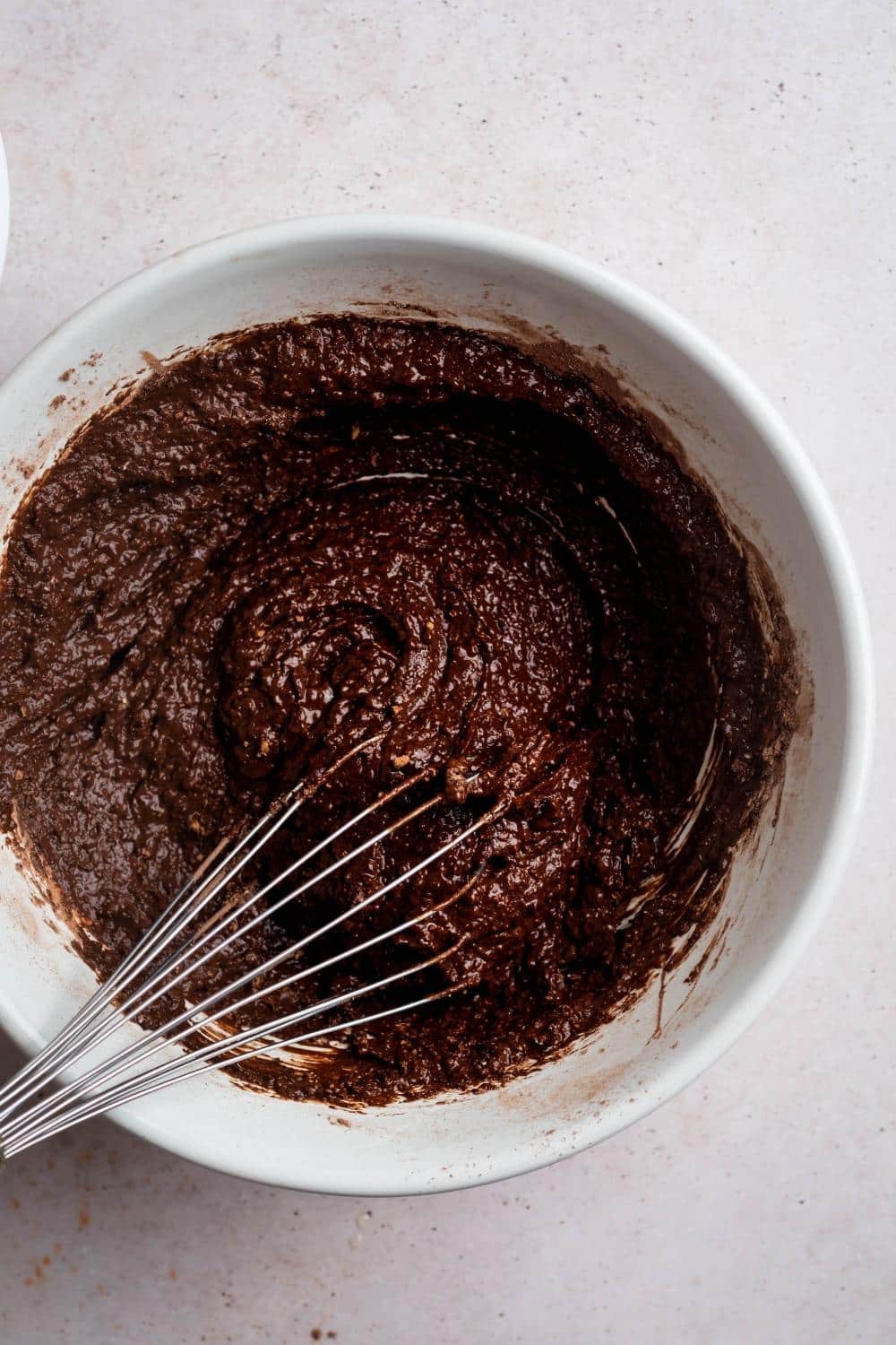 A bowl of chocolate donut batter with a whisk submerged in it.