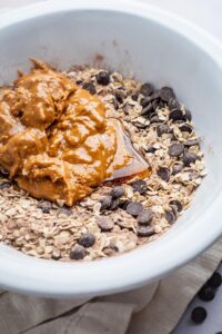 Peanut butter and honey on top of oats, protein powder, and chocolate chips in a bowl.