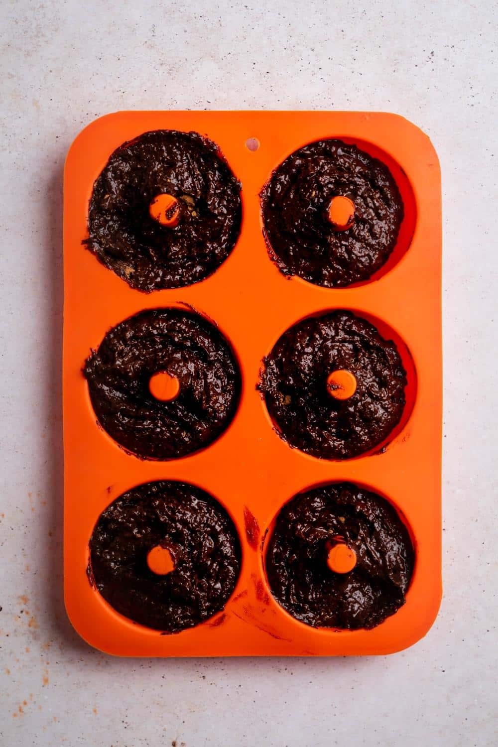 Chocolate donut batter in a six donut slotted silicone donut tray.