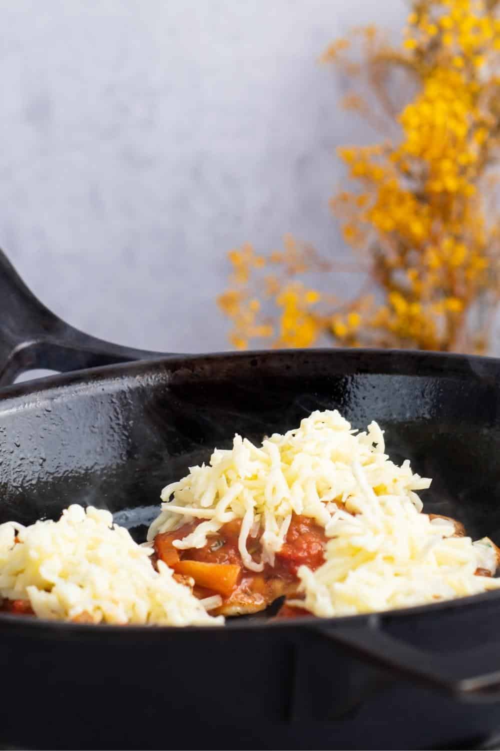 Three pieces of chicken in a skillet with sauce and shredded cheese on top.