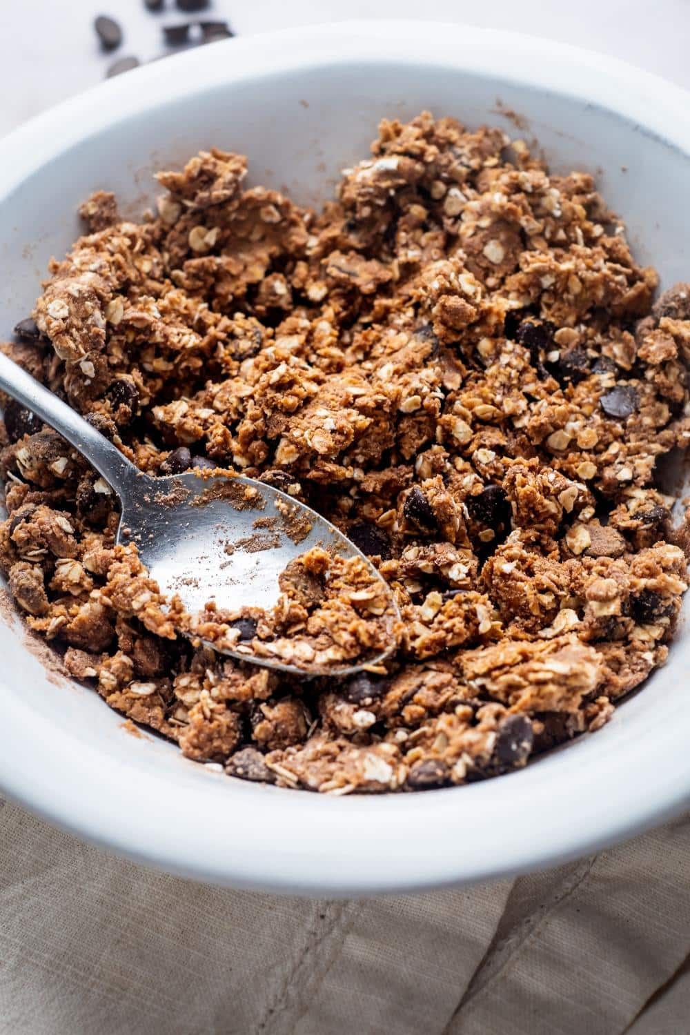 A bowl of oats, honey, chocolate chips, protein powder, and peanut butter in a white bowl.