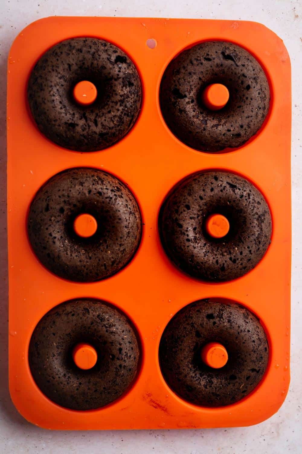 Six chocolate donuts in an orange silicon donut tray.