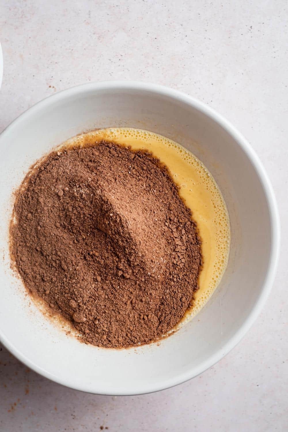 Chocolate protein powder in a white bowl with an egg mixture in it.