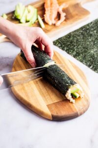 A hand slicing a rolled up sushi roll in half.