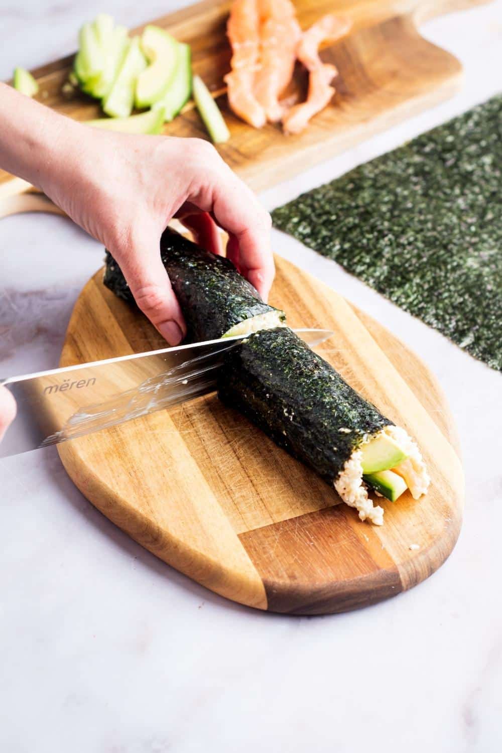 A hand slicing a rolled up sushi roll in half.