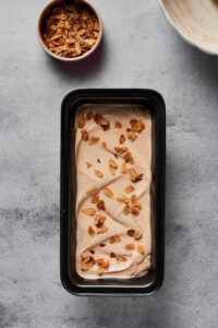 A rectangular tin with almond ice cream topped with toasted almonds. Behind it is a bowl of toasted almonds.