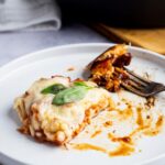 A piece of keto chicken parmesan with a piece cut out of the front of it on a white plate.