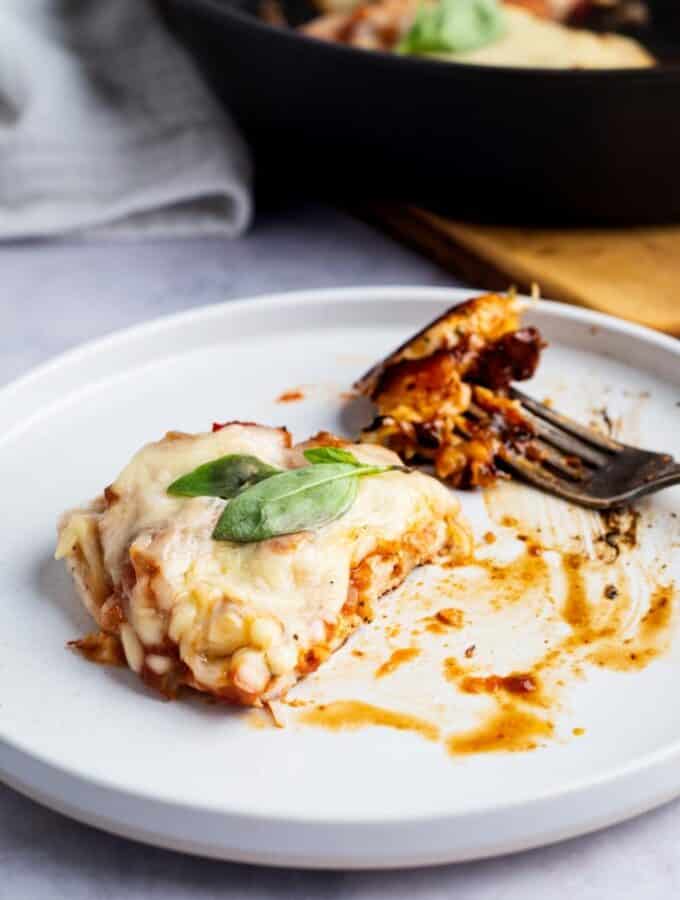 A piece of keto chicken parmesan with a piece cut out of the front of it on a white plate.