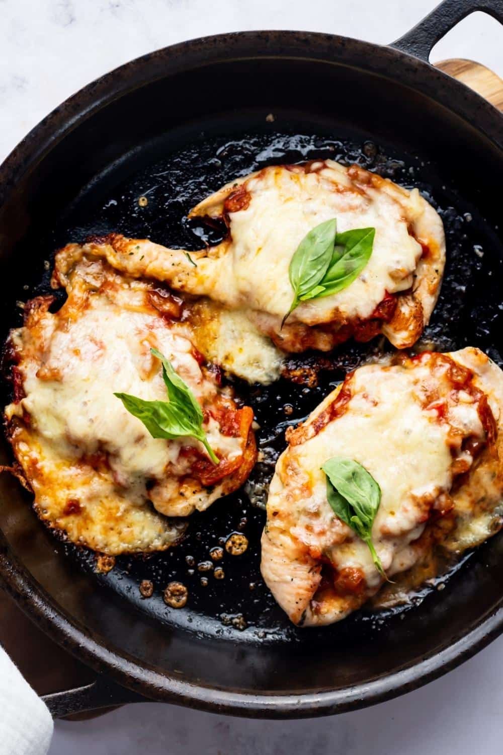 Three pieces of keto chicken parmesan in a skillet.