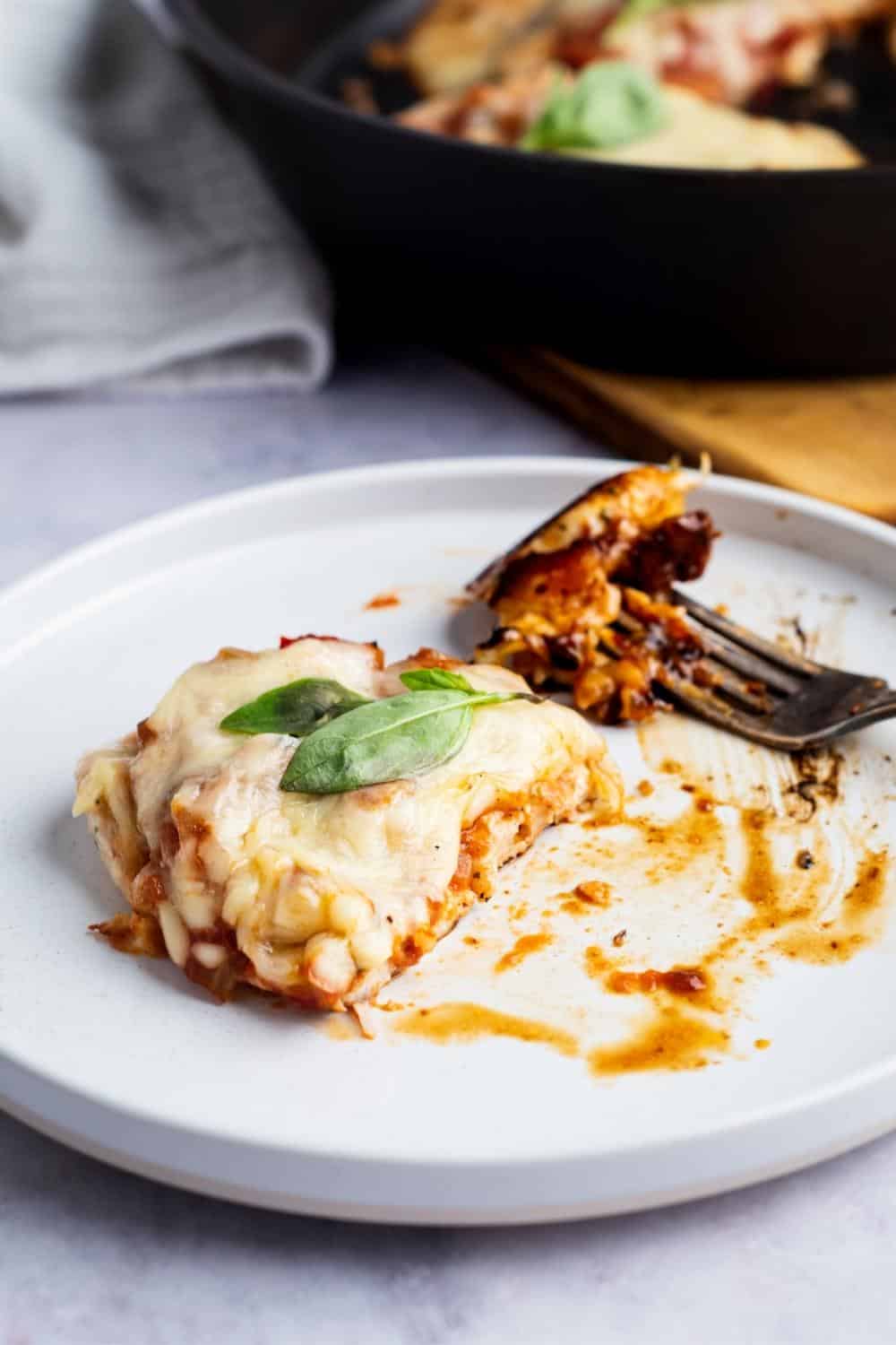 A piece of keto chicken parmesan with a piece cut out of the front of it on a white plate.