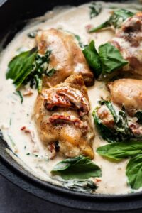 Sun dried tomatoes on top of chicken thighs that are in a cream sauce with spinach in a pot.