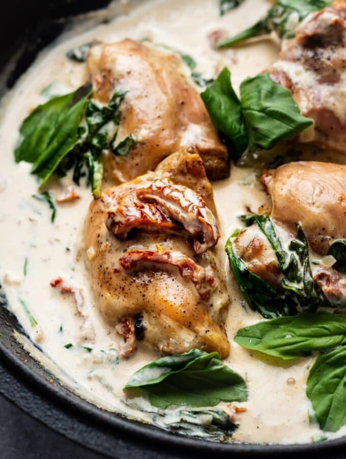 Sun dried tomatoes on top of chicken thighs that are in a cream sauce with spinach in a pot.