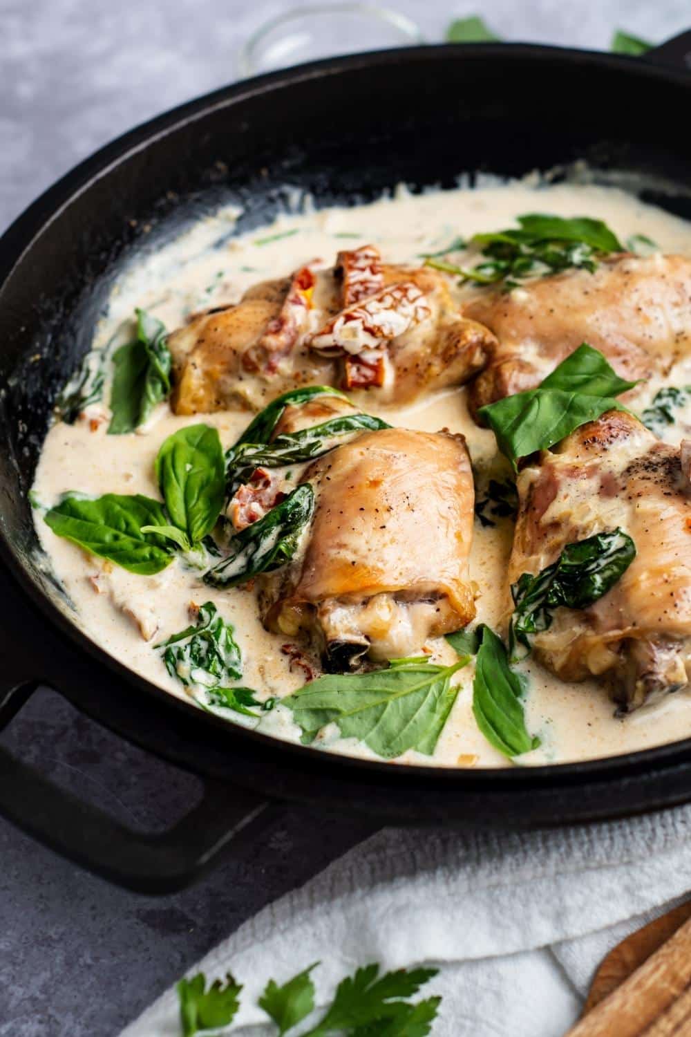 Four chicken thighs with spinach and sun dried tomatoes in a cream sauce in a pot.