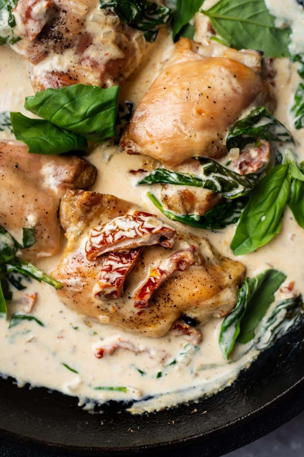 Sun dried tomatoes on a chicken thigh that is in a cream sauce with spinach in a pot.