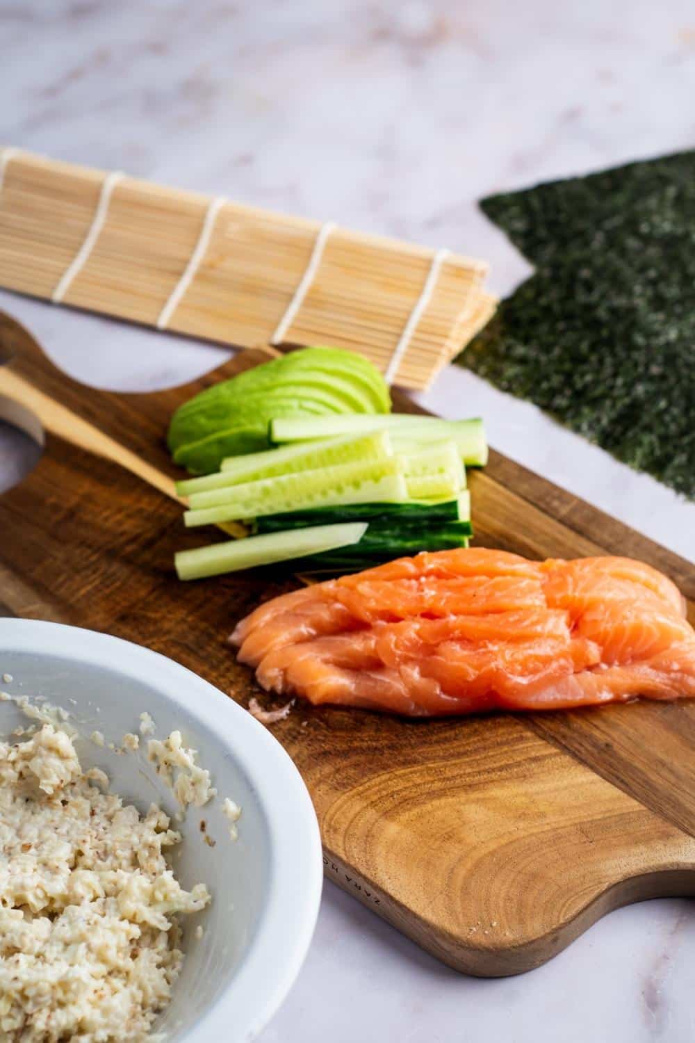 A wooden cutting board with salmon and sliced cucumber on it.