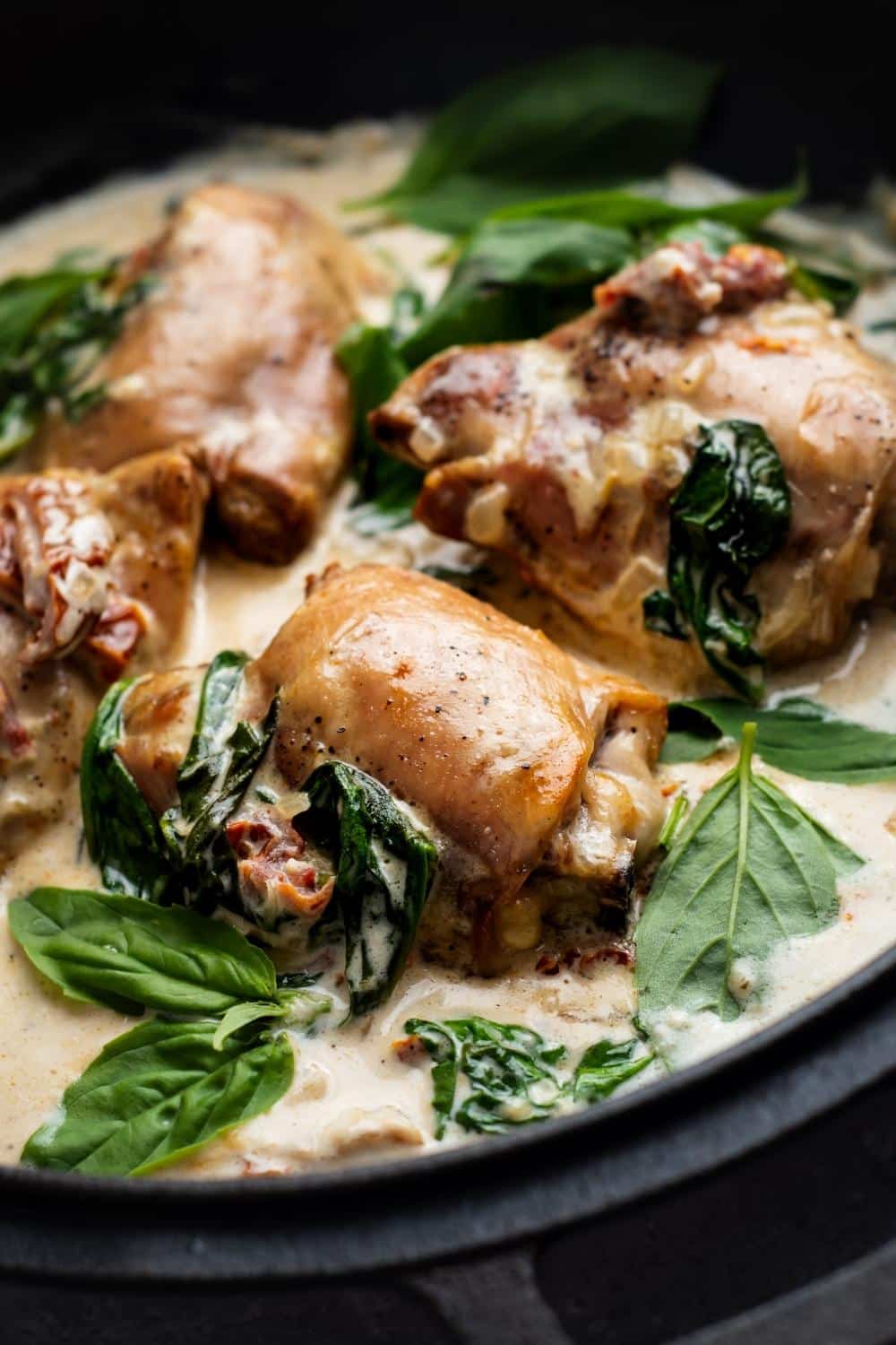Part of a pot with a cream sauce, chicken thighs, spinach, and sun dried tomatoes in it.