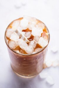 A straw and ice cubes in a glass that is filled with protein coffee.