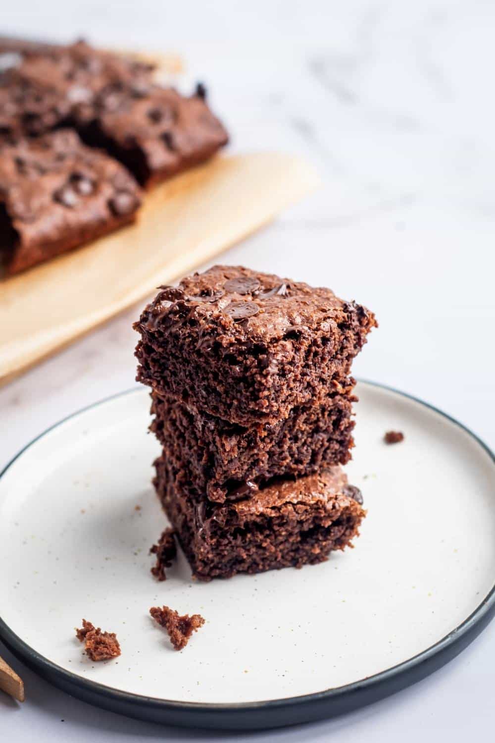 Three brownies stacked on top of one another on a white plate.