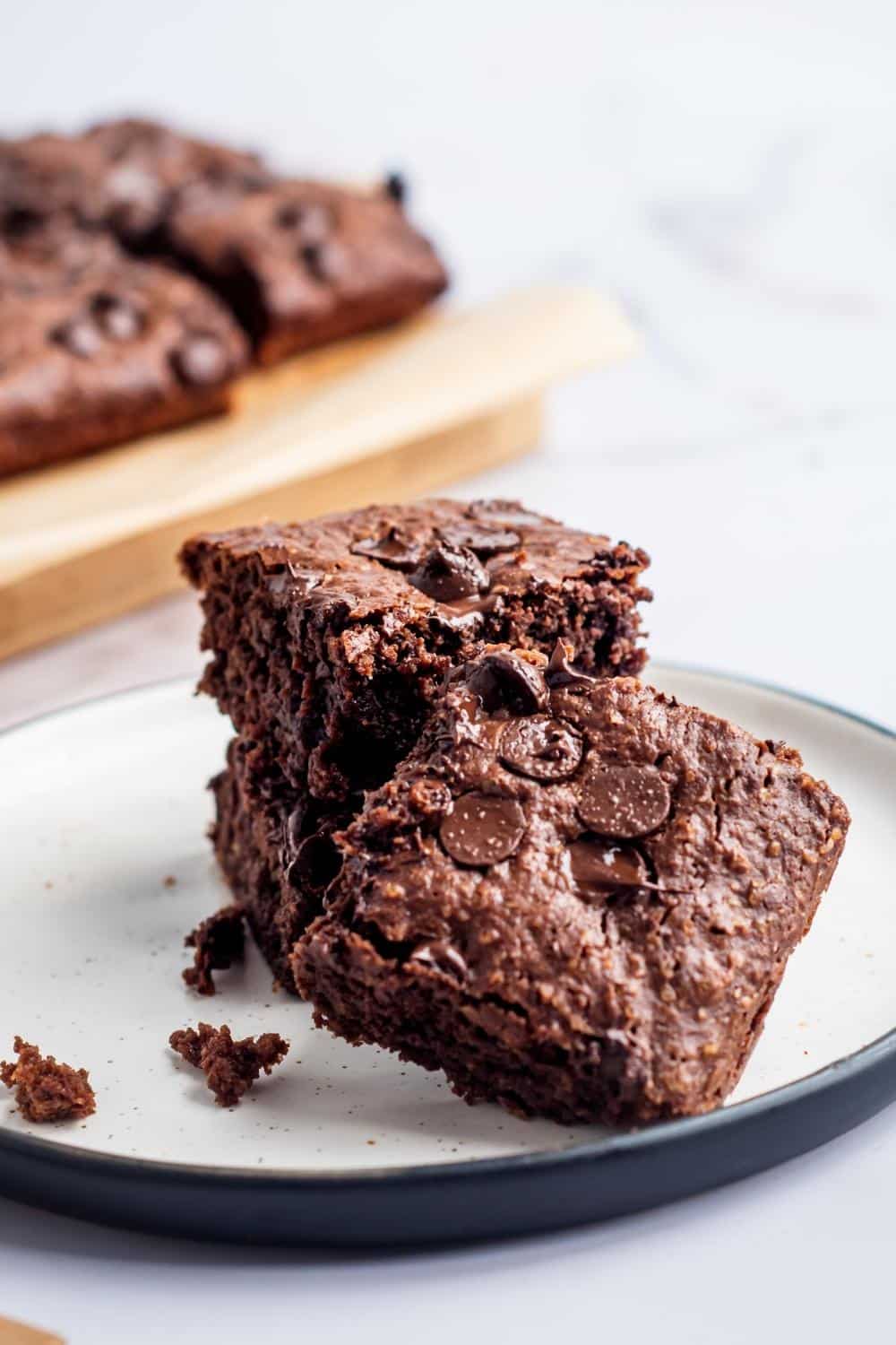 A brownie square in front of a stack of two brownies on a white plate.