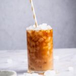 A glass of protein coffee on a white counter with ice cubes on it.