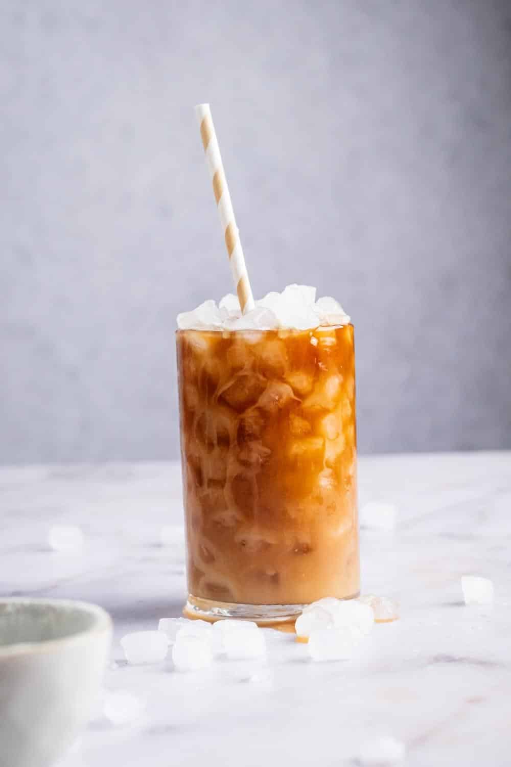 A glass of protein coffee on a white counter with ice cubes on it.