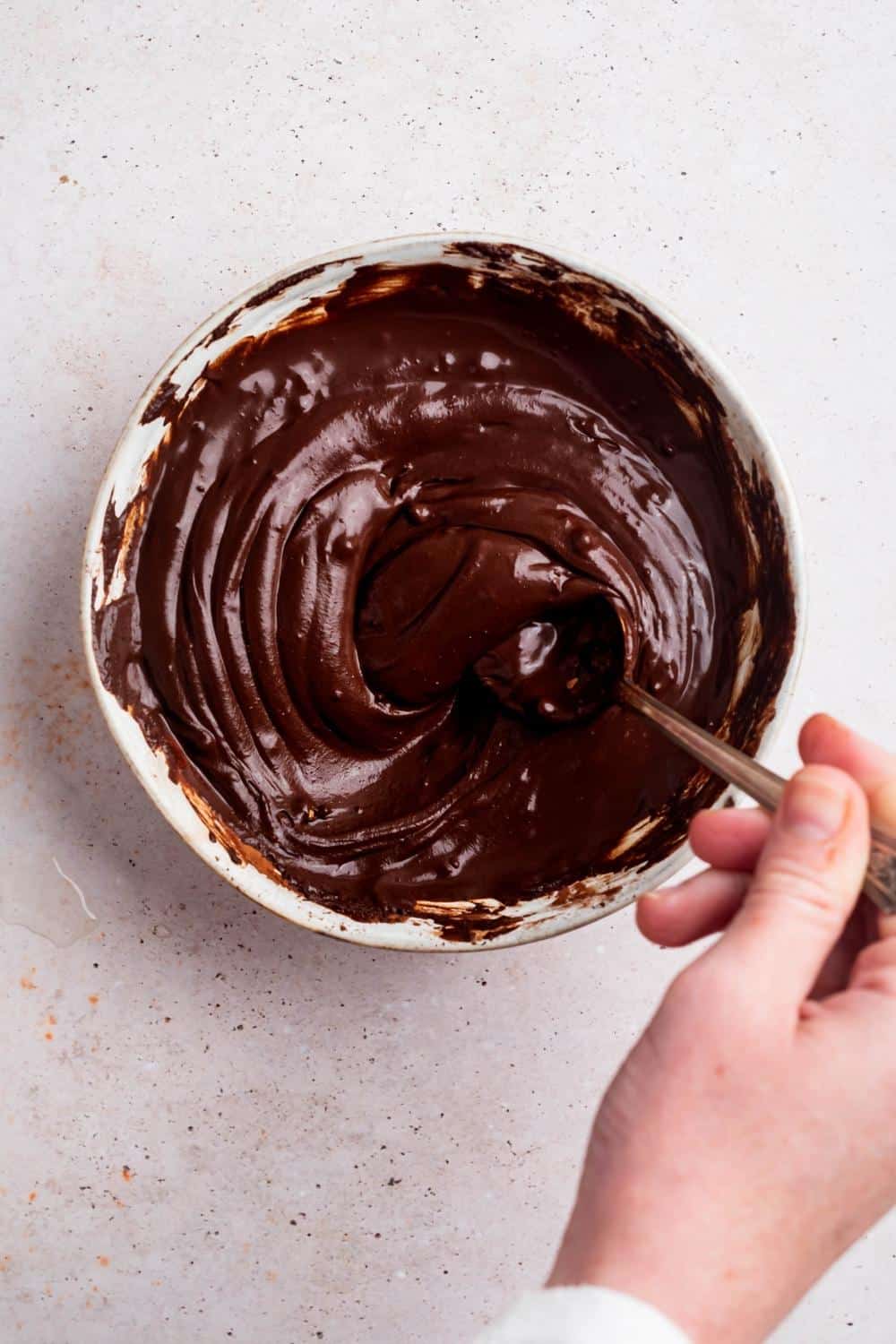 A hand mixing a chocolate glaze with a spoon.