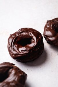 Chocolate protein donut on a white counter with part of two donuts on each side of it.