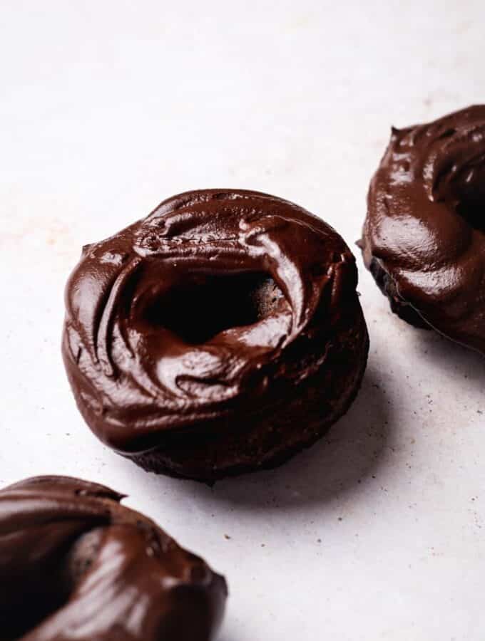 Chocolate protein donut on a white counter with part of two donuts on each side of it.