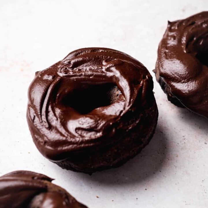 Chocolate protein donut on a white counter with part of two donuts on each side of it.